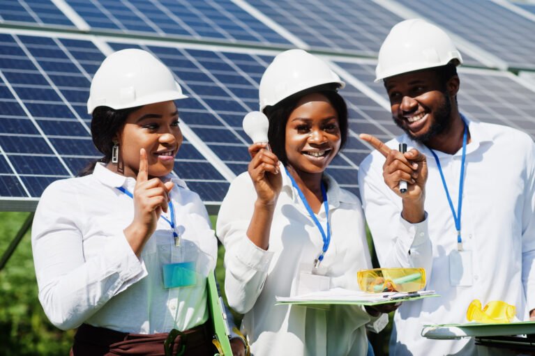 African american technician checks the maintenance of the solar panels. Group of three black engineers meeting at solar station. Hold led bulb.