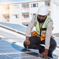 African engineer man, screwdriver and solar panel on roof for maintenance, industry or thinking in city. Technician, builder and tools for photovoltaic tech, helmet and sustainable renewable energy.